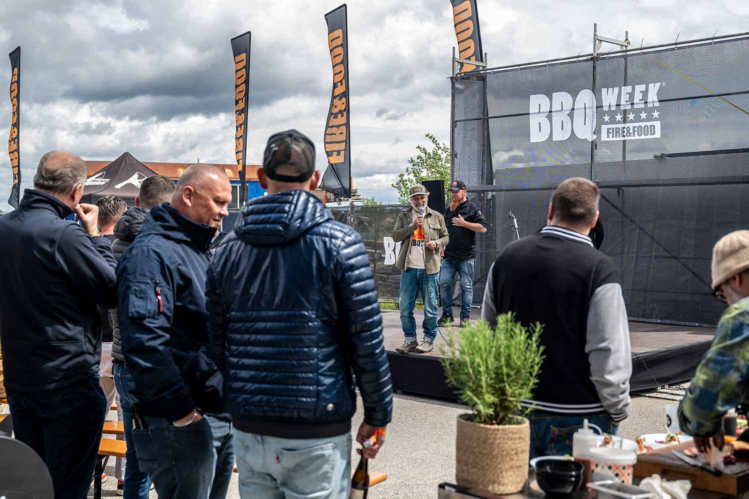 People watching a BBQ event on stage with banners in the background.