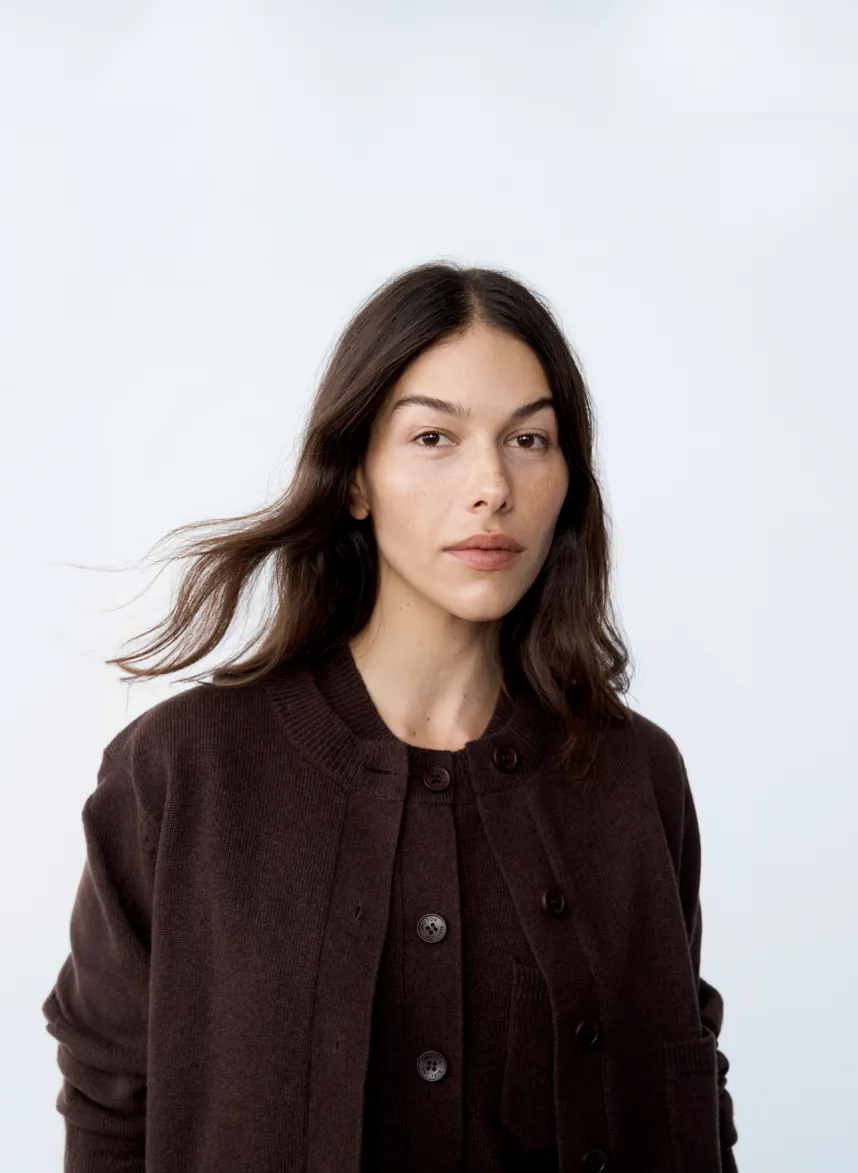 Woman with long hair wearing a dark cardigan, against a light background.