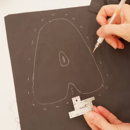 Adding seam allowance on a letter Shape A drawn with a white heat erasable fabric marker on dark fabric
