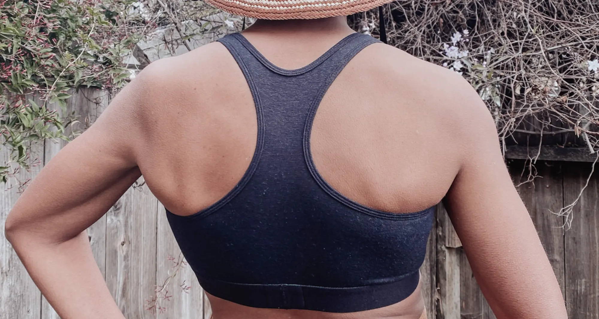 The back of a woman wearing a black bralette and a cream/brown sunhat.