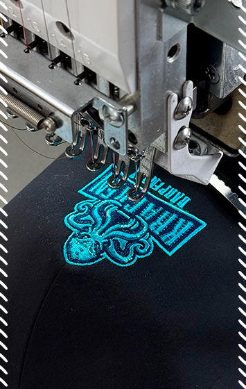 Industrial embroidery machine stitching a bright turquoise logo onto black fabric using satin stitch technique