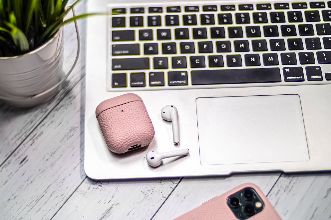 pink genuine leather airpods laying on a macbook air on a grey wooden table top