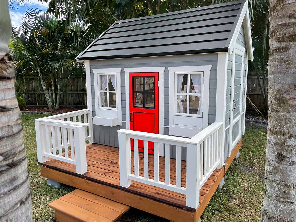 Kids Wooden Playhouse Boy Cave With Black Metal Roof, Grey Walls and Red Half Glass Door in a backyard By WholeWoodPlayhouses