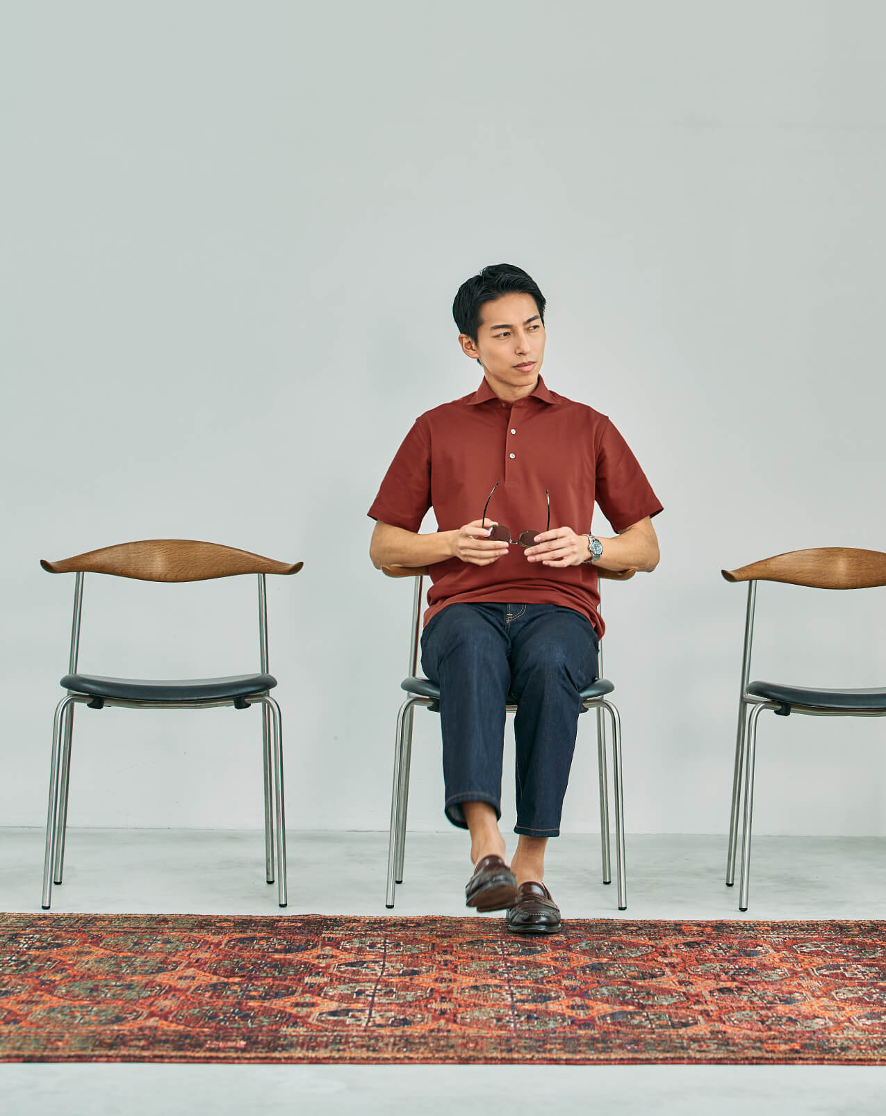 Man in a brown polo shirt looking down thoughtfully by a window.