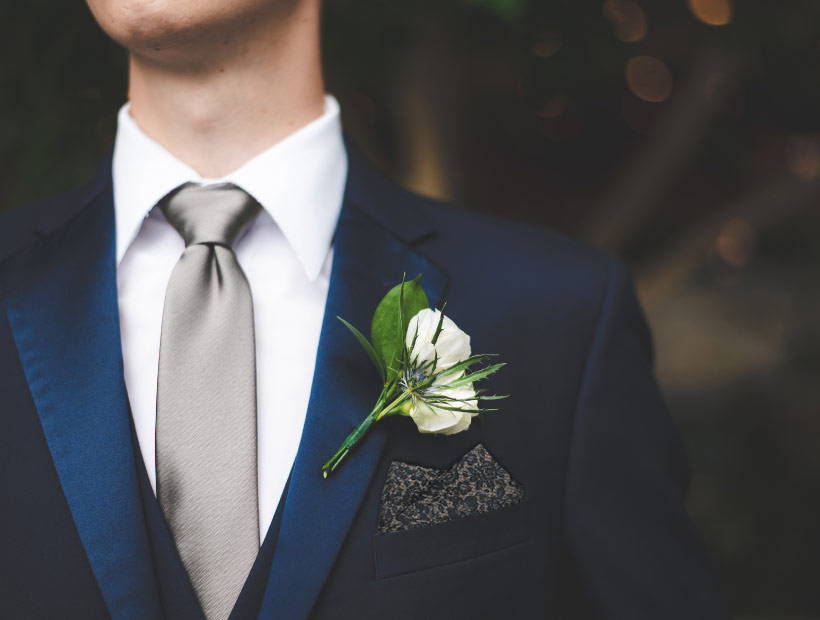 A man dressed formally with a suit, tie, pocket square and boutonniere