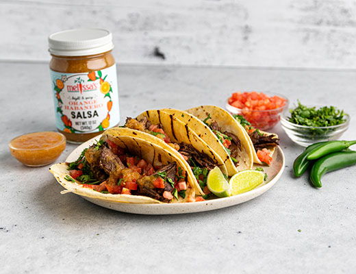 Three tacos with salsa, tomatoes, cilantro, jalapeños, and a jar of salsa.