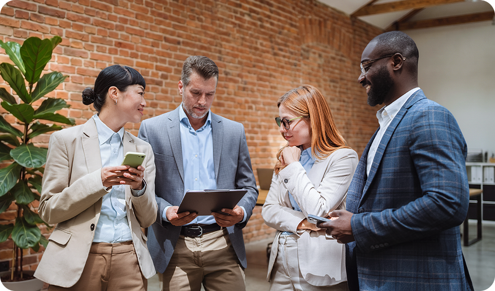 Four professionals discussing work in a modern office setting with brick walls.