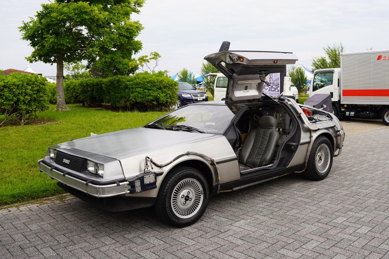 A silver DeLorean car with gull-wing doors parked on a driveway.