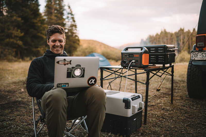 A man charges cooler and tablet with Jackery Explorer 1000 solar generator on a campground.