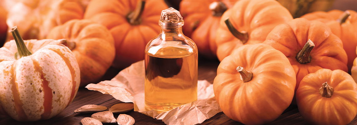 Pumpkins surrounding a small glass bottle with liquid.