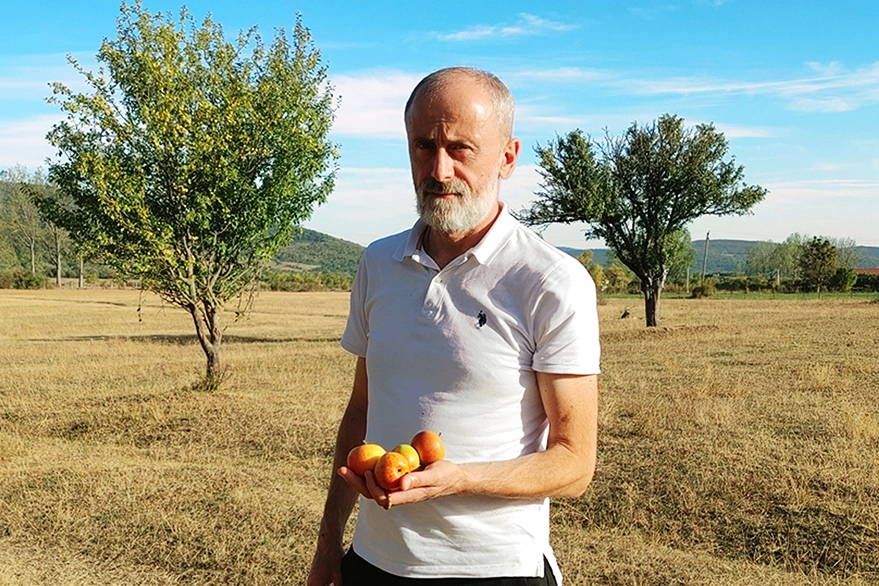 Farmer Malxhaz holding freshly harvested apples in an orchard in Tianeti, Georgia, demonstrating the local agriculture and fresh ingredients.
