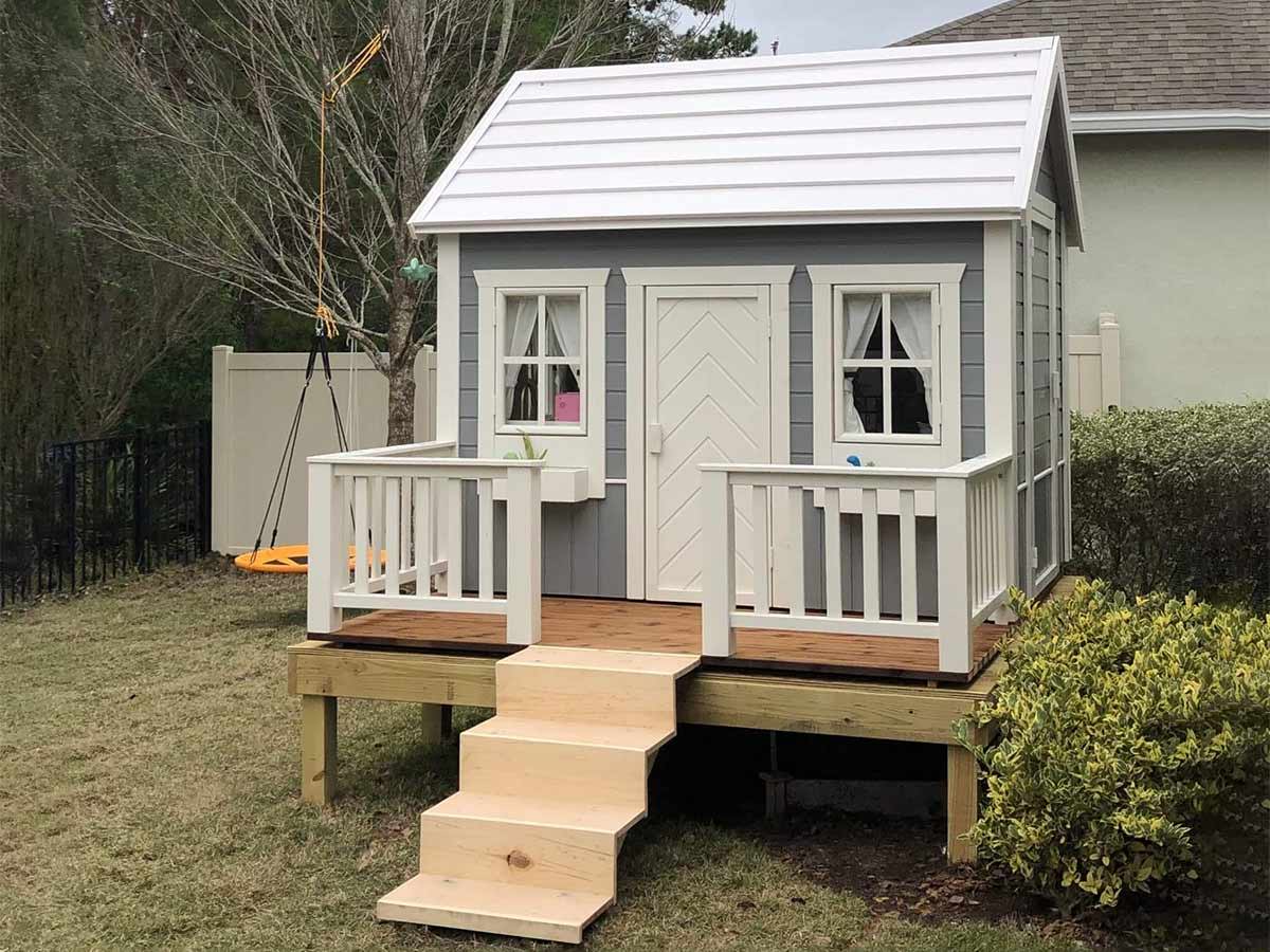 Custom wooden playhouse on stilts with ladder in the backyard by WholeWoodPlayhouses