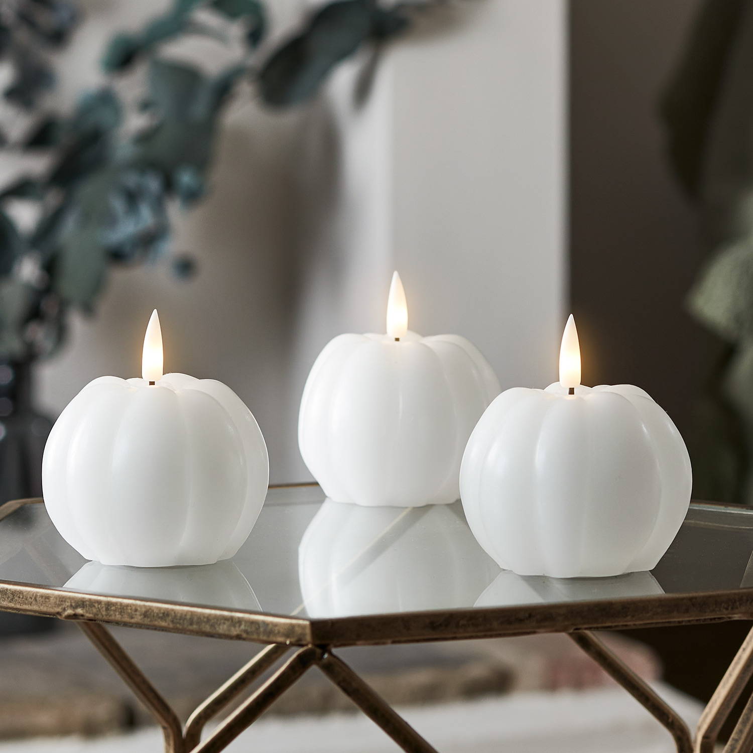 Trio of white pumpkin LED candles on a glass living room table