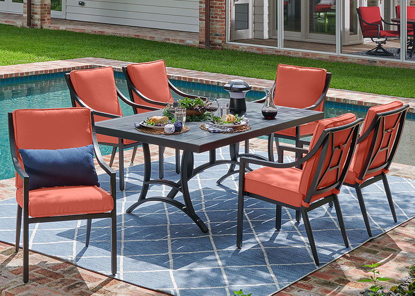 Outdoor dining set with orange chairs by a poolside.
