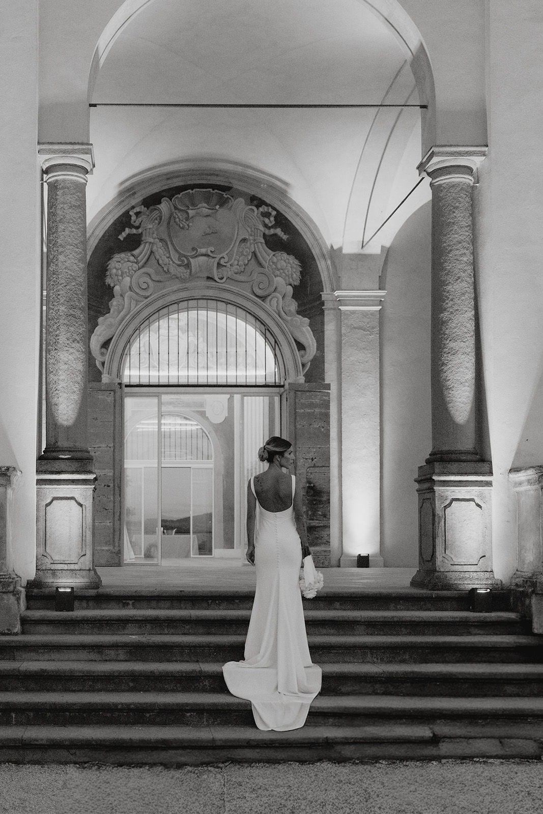 A woman in a white dress standing on steps of a grand entrance.