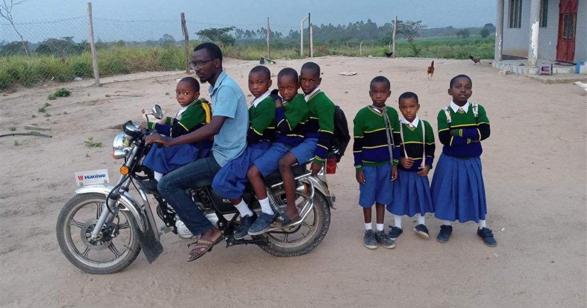 A man on a motorcycle with children in school uniforms.