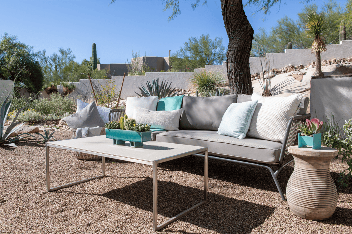 An outdoor sitting area with sofa and coffee table comes alive with pastel turquoise color accents complimenting the surrounding landscaping. 