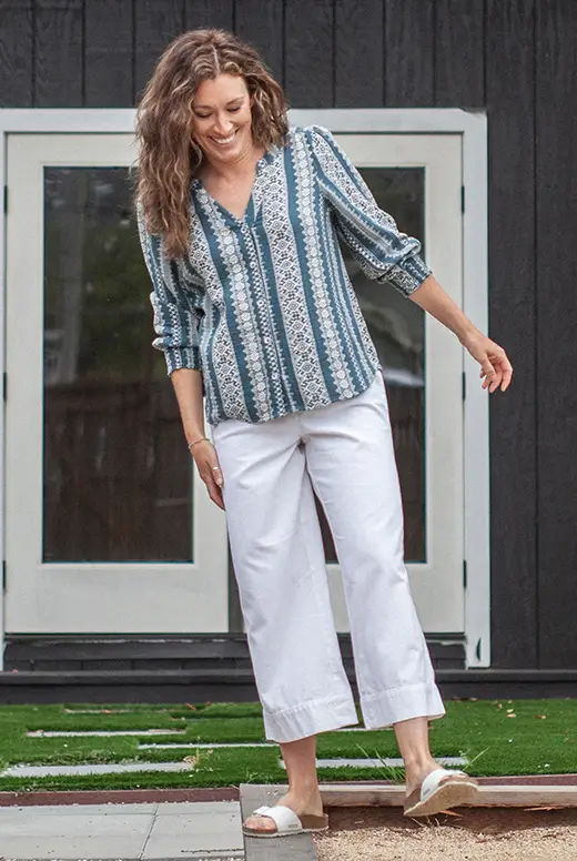 Woman in patterned blouse and white pants walking outdoors.