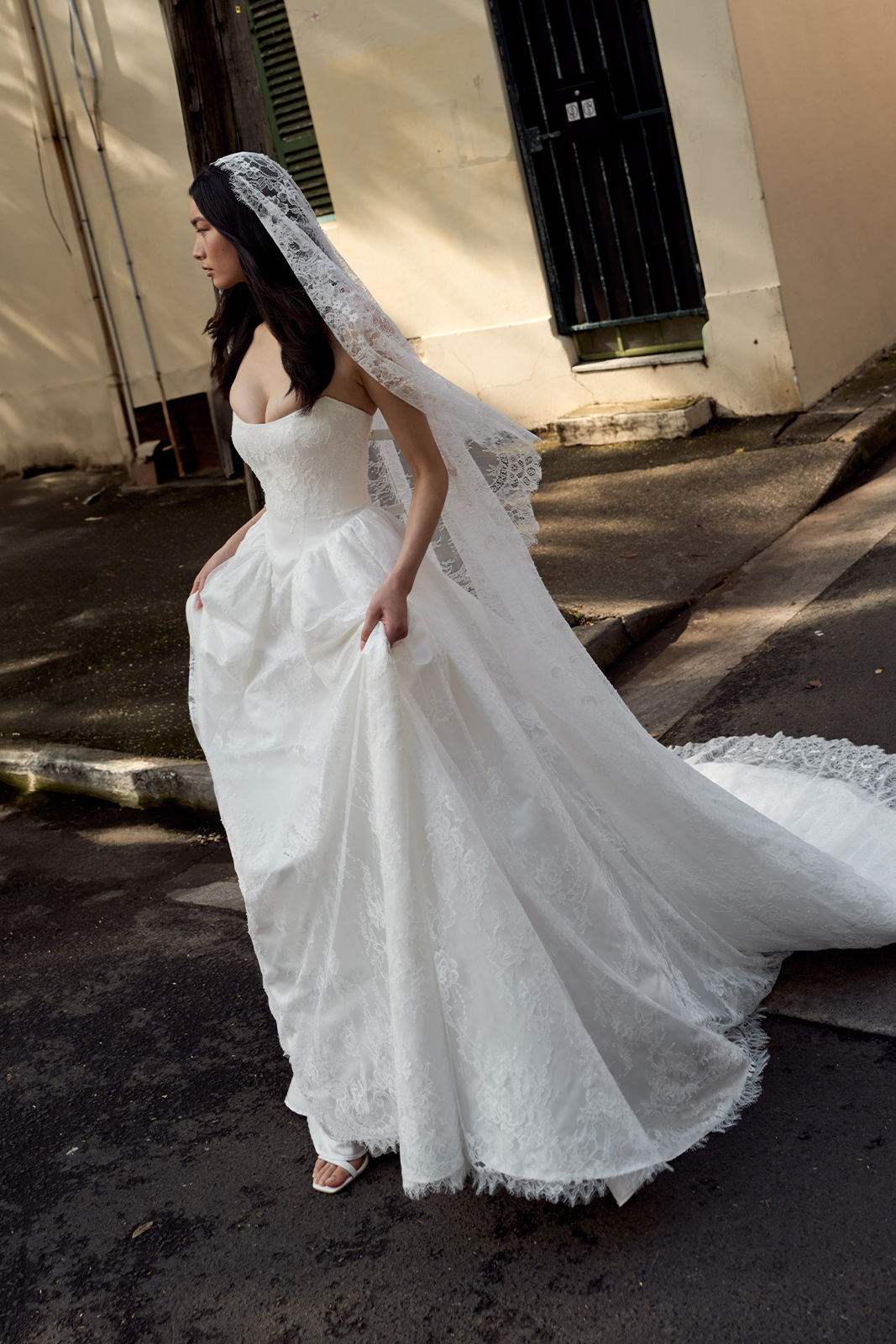 Bride in a white wedding dress with a veil, walking outdoors.