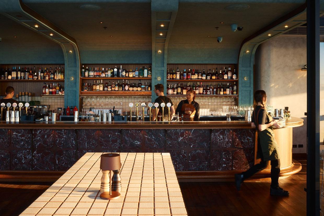 A modern bar with staff and shelves of bottles.