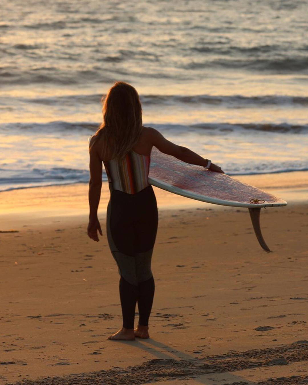  Image of surfer walking towards the Ocean holding a surfboard at sunset.
