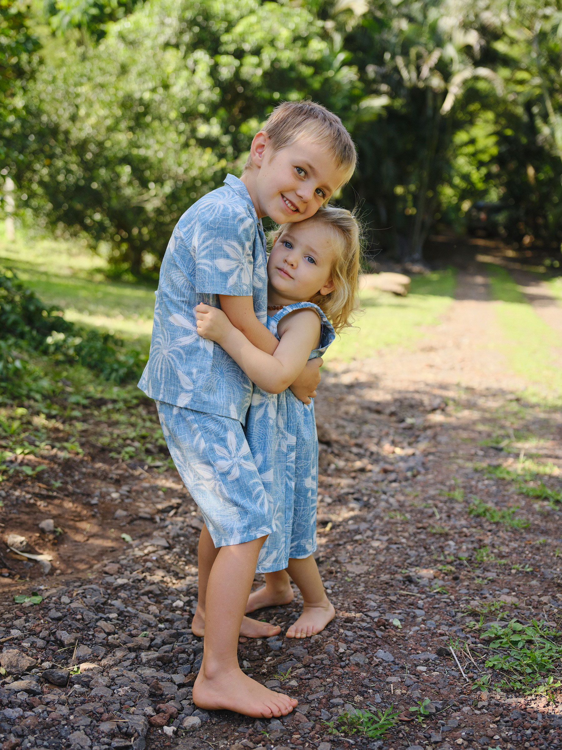 Two children in matching blue outfits hugging outdoors.