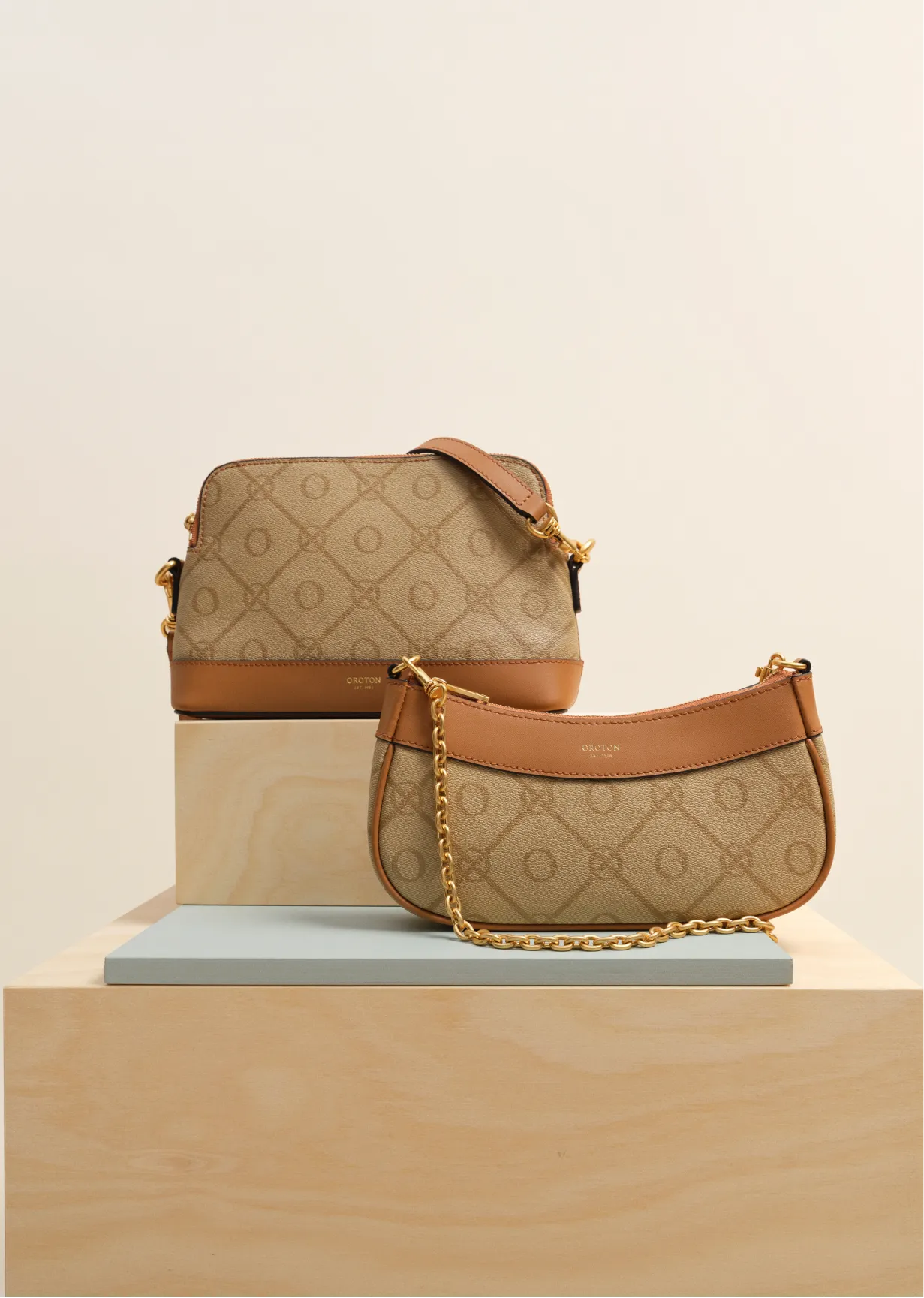 Two stylish handbags displayed on a wooden stand against a neutral background.