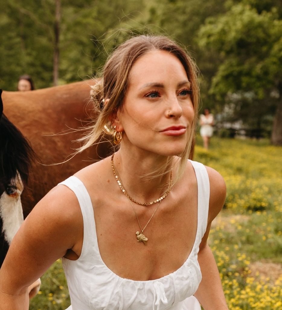 Woman in a white dress outdoors with a cow in the background.