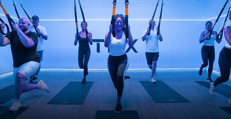 Group workout session with TRX straps in a blue-lit gym.