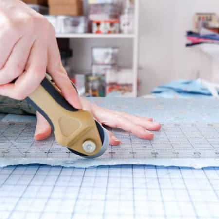 rotary cutter cutting blue fabric on a transparent cutting mat using a ruler