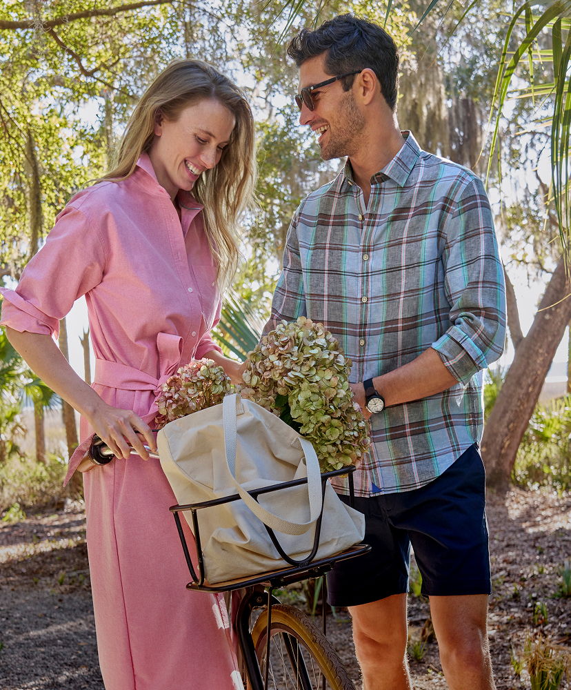 A couple smiling while interacting near a bicycle with flowers in a park.