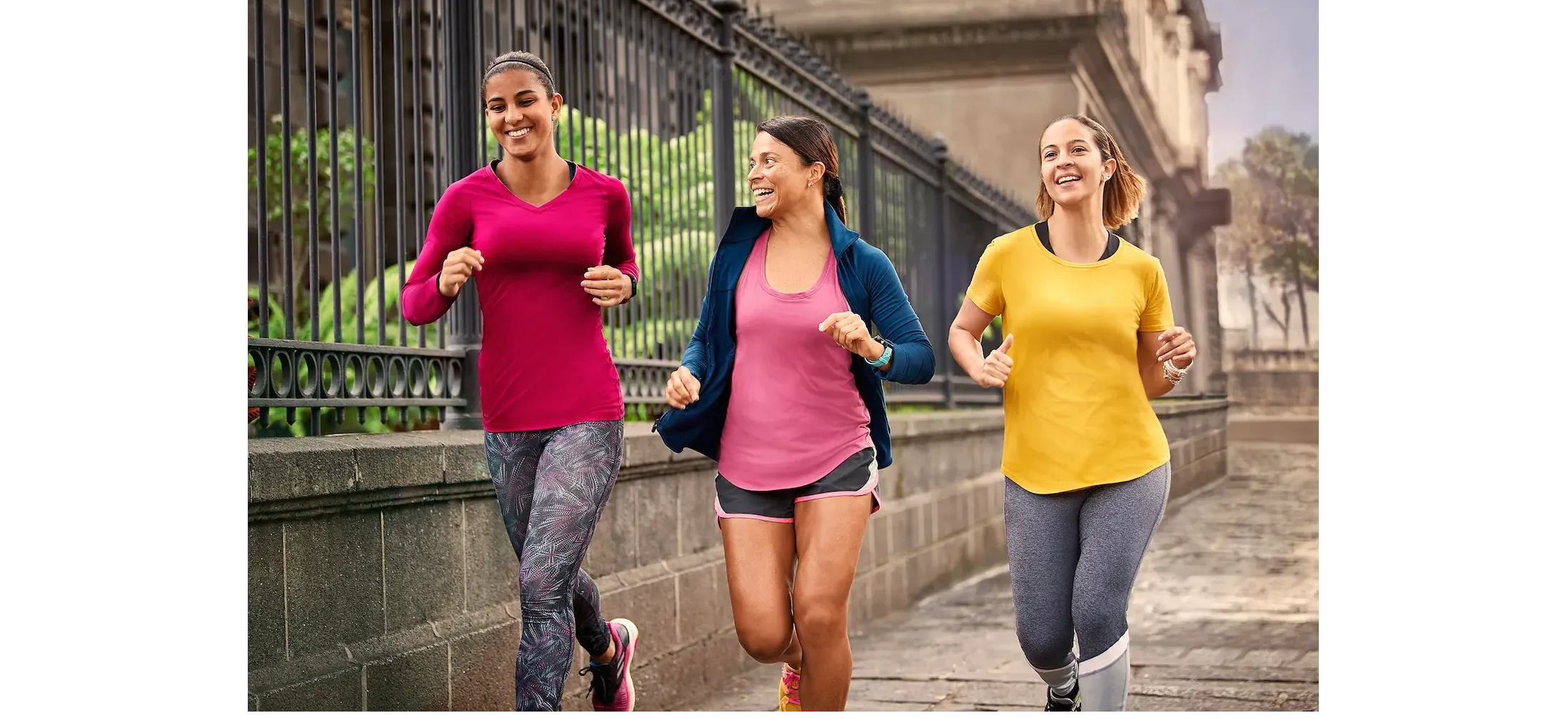 Three women running down a sidewalk wearing GPS running watches