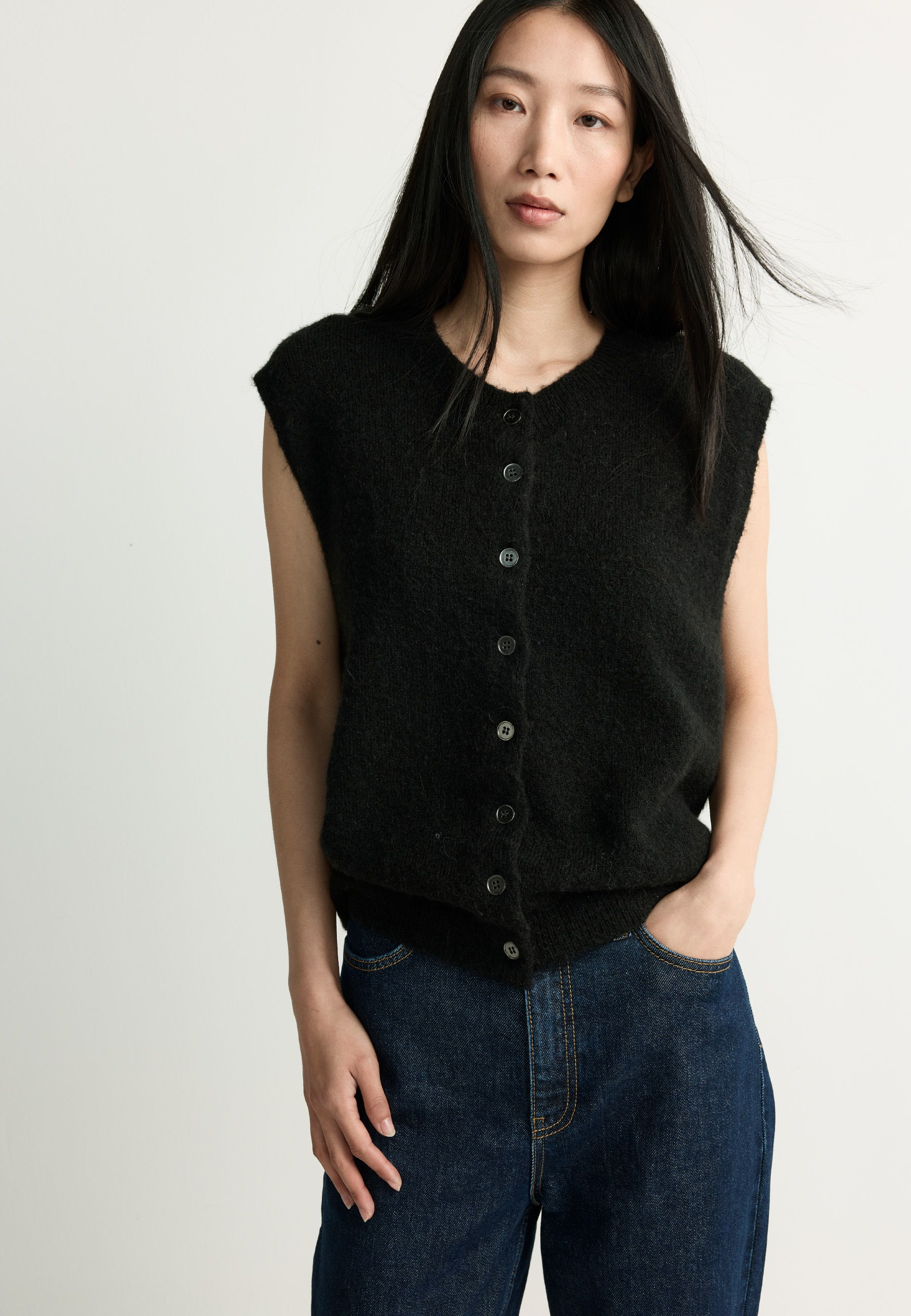 Person wearing a black sleeveless top and blue jeans, standing against a light background.