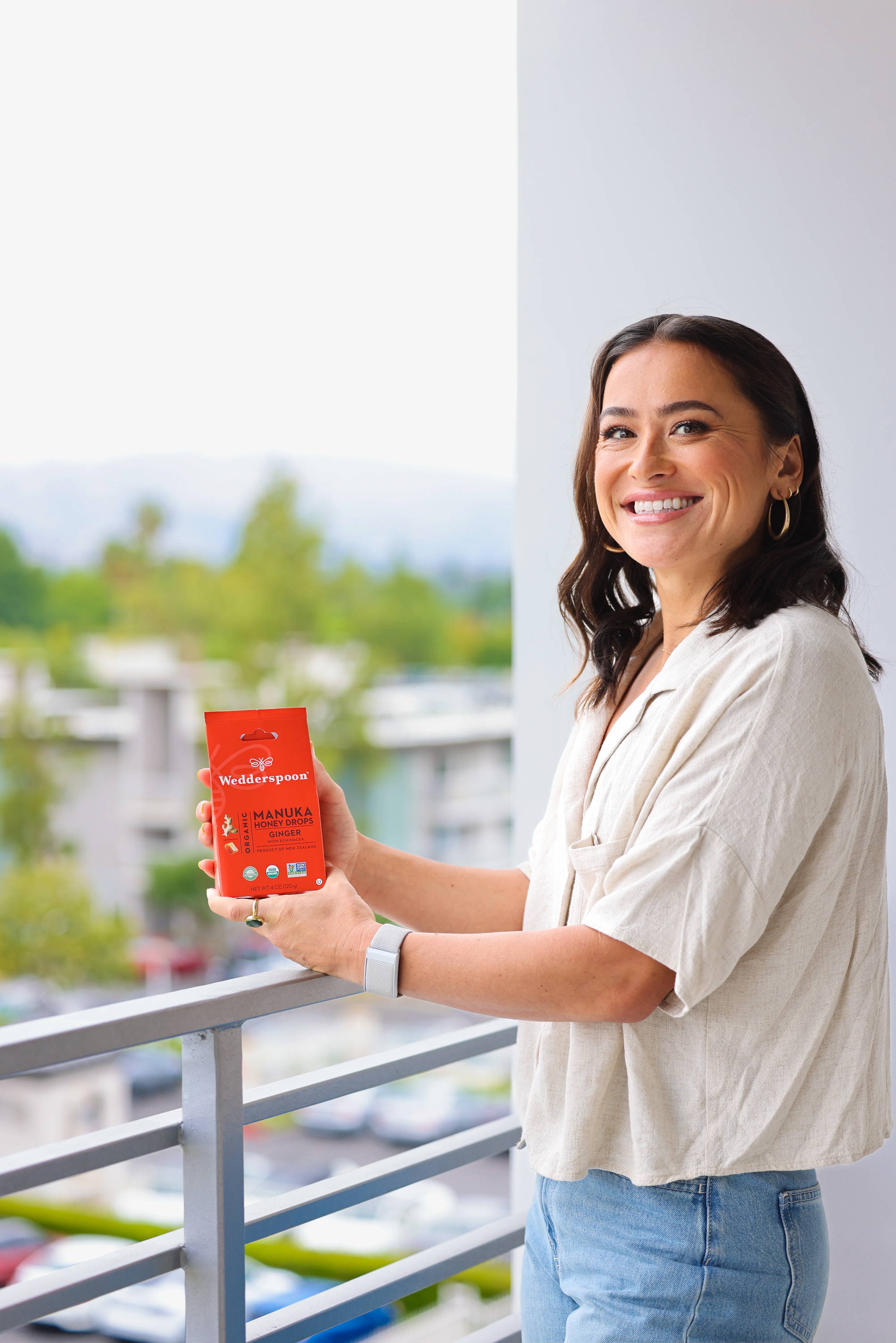 Ali Riley, professional soccer player, holding a box of Wedderspoon Organic Manuka Honey Drops - Ginger, a delicious and energizing snack for athletes and health-conscious individuals.