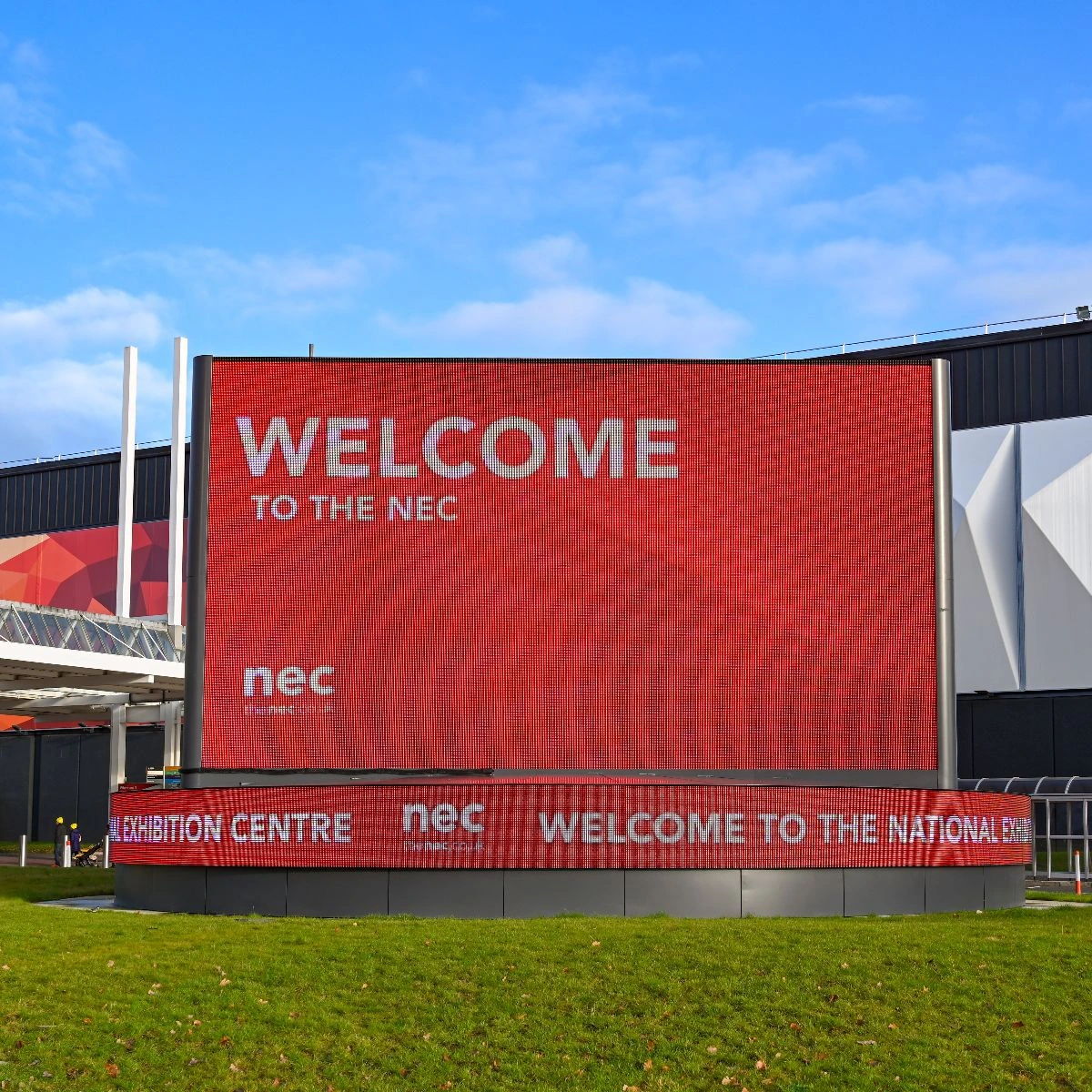 Welcome sign at the NEC with blue sky and green grass.