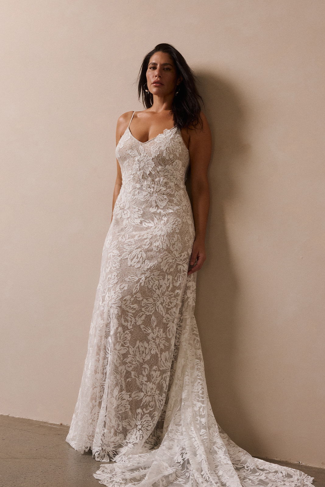 Woman in a lace wedding dress posing against a neutral background.