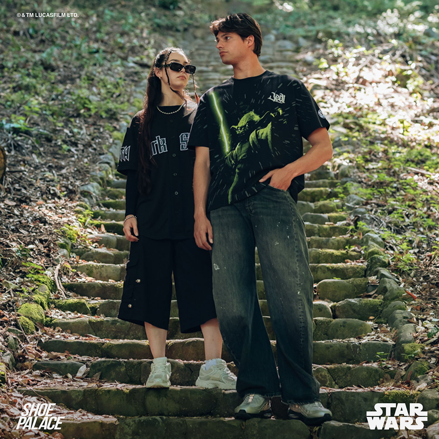 Two individuals in casual attire standing on stone steps in a wooded area.