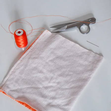 A sewn orange seam with orange thread and thread sips and a hand needle