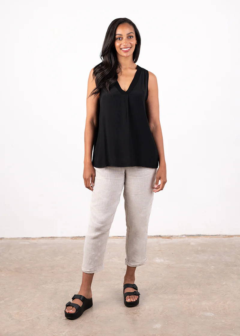 A model wearing a black v sleeveless top with off white trousers and chunky black slides