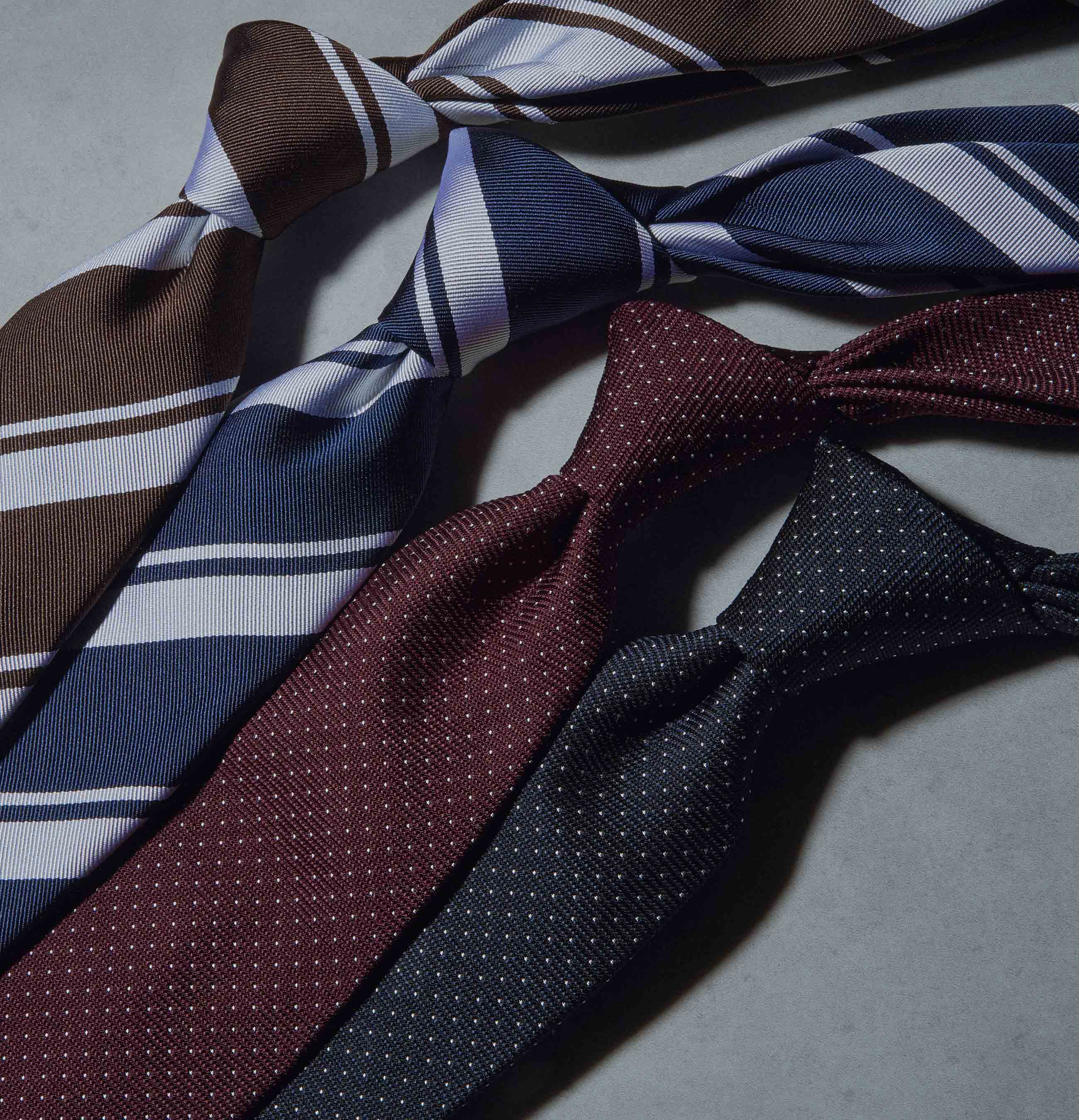 Four neckties in various colors and patterns on a gray surface.