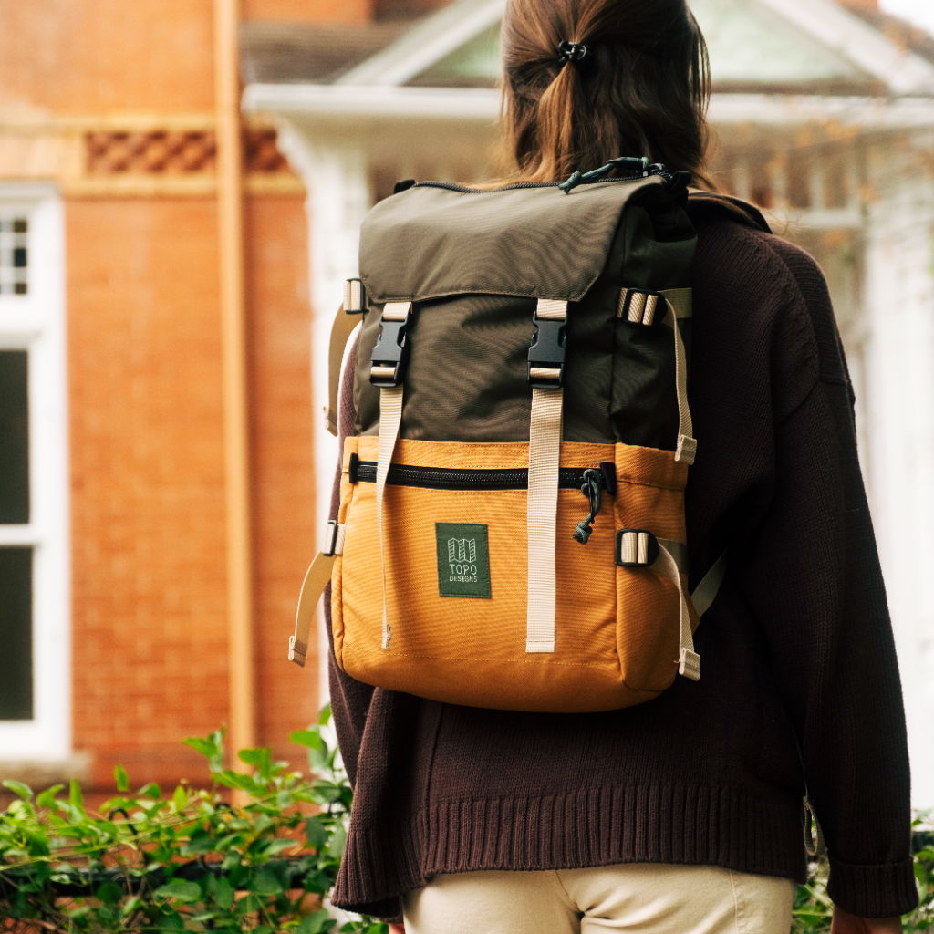 Person wearing a backpack standing in front of a building with greenery.