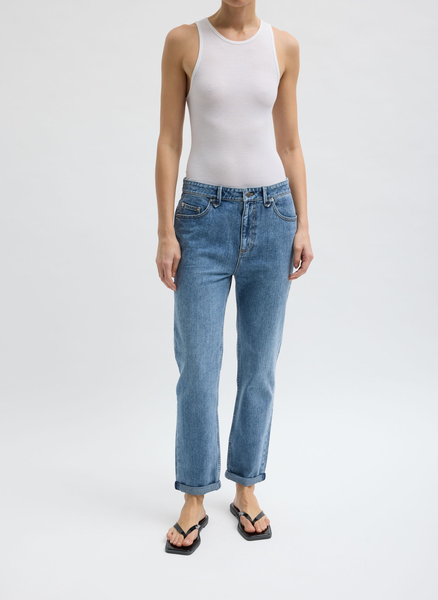 Person wearing a white tank top, blue jeans, and flip-flops.