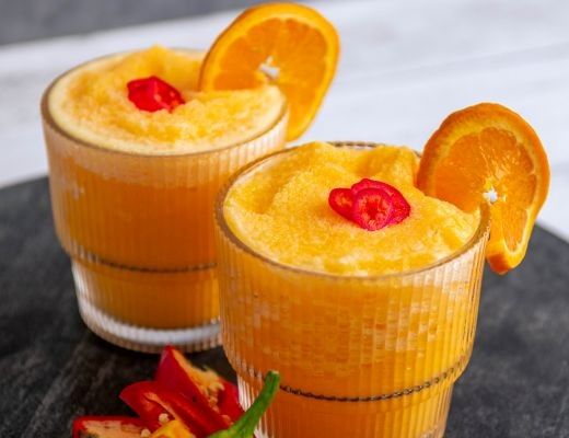 Two orange slush drinks with cherries and orange slices on top.