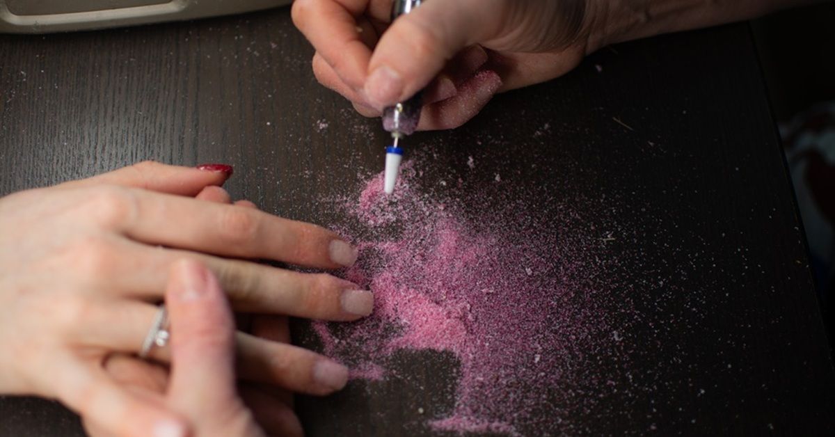 A person applying pink glitter to a client's nails.