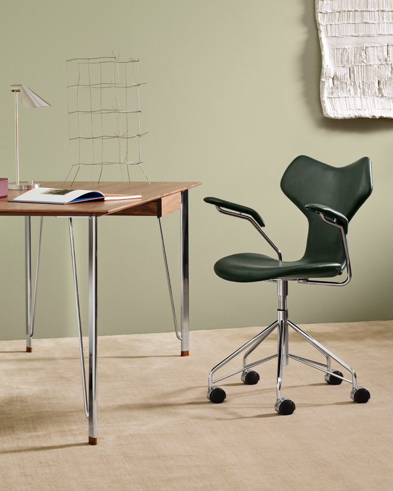 A green Grand Prix ergonomic chair beside a wooden desk in a minimalist setting.