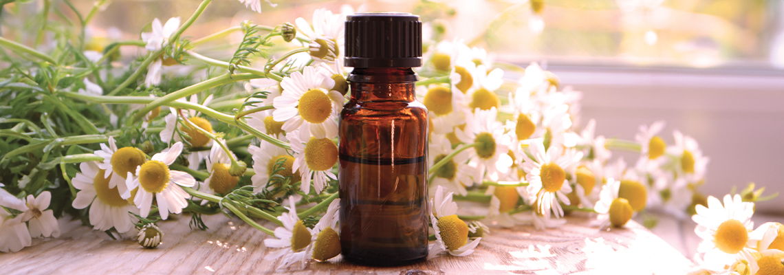 A small bottle surrounded by flowers on a soft surface.