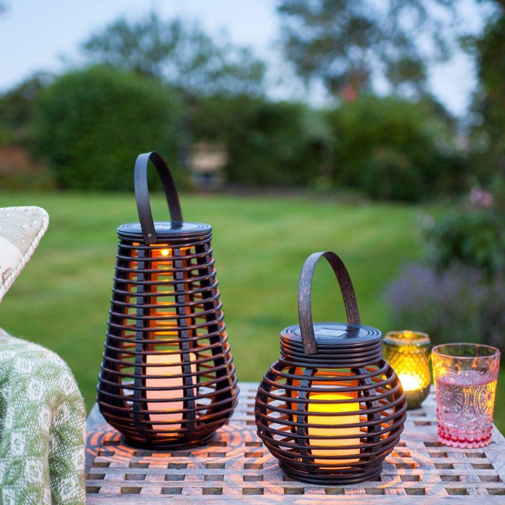 Black solar lanterns on an outdoor table over looking a garden.