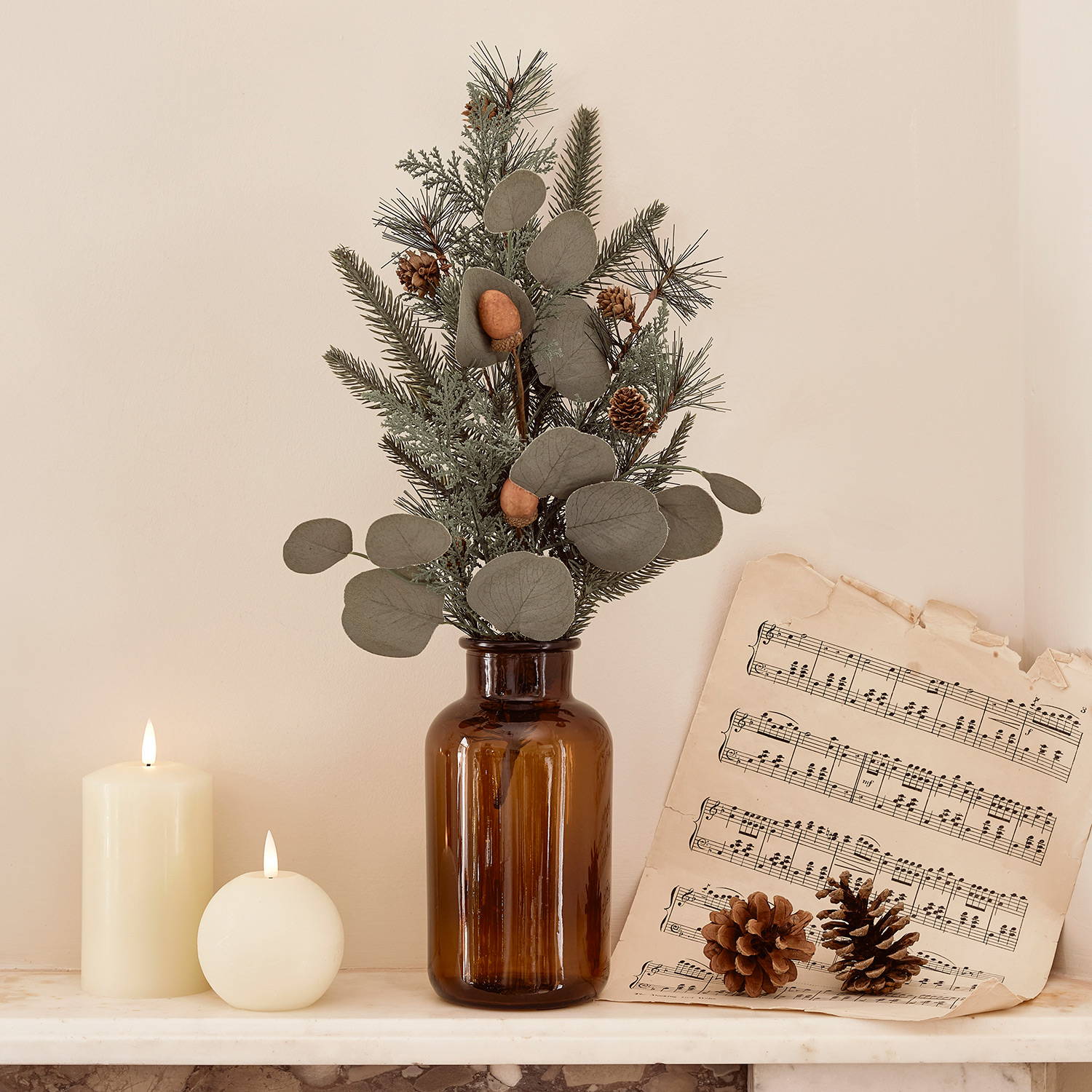 Artificial miniature pinecone tree and TruGlow® candles on a mantlepiece with a song sheet.