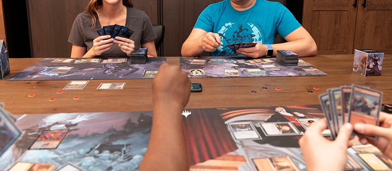how to play magic the gathering commander - People playing a tabletop game with cards and game boards.