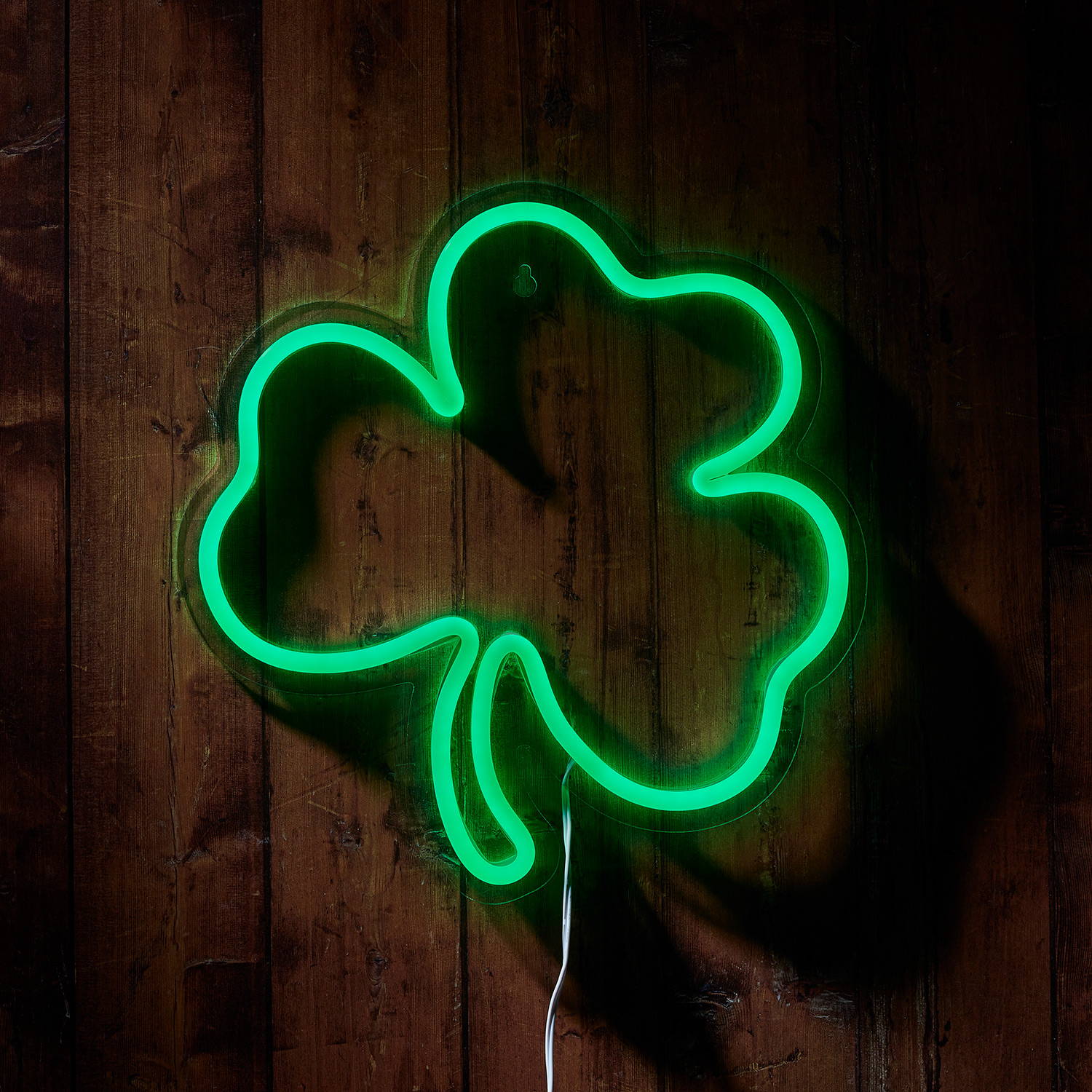 A neon green shamrock wall light against a dark wooden wall.